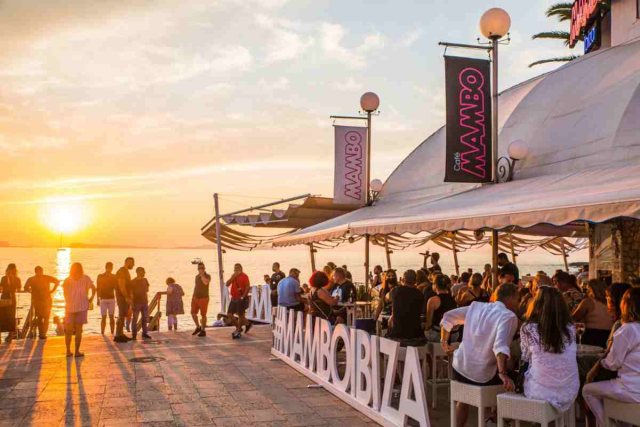 Gente reunida en Café Mambo disfrutando del atardecer sobre el mar en Sant Antoni.